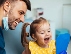 Happy child receiving a checkup from a male kids' dentist, holding a mirror during the dental visit